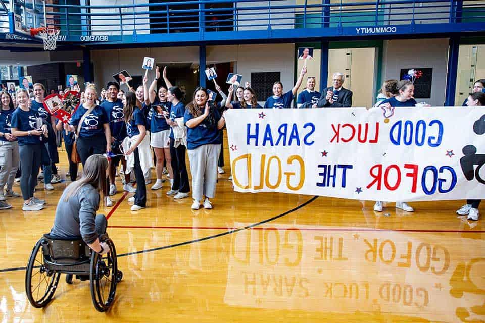 A large group of well-wishers present Sarah Adam with a banner that reads "Good luck, Sarah! Go for the gold!"